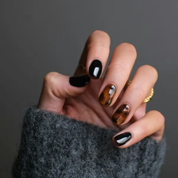 A hand shows glossy black and tortoiseshell nail art.