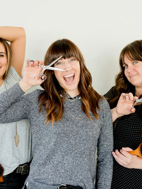 Three salon professionals pose together with their scissors and brushes.