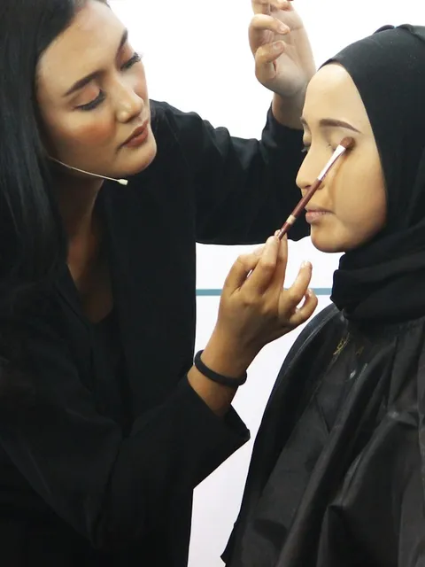 A makeup educator demonstrates eye makeup on a model during a class.